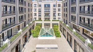 A modern multi-story building with a central courtyard featuring a glass-roofed swimming pool, surrounded by balconies with railings. - Zenitude Hôtel-Résidences Val d'Europe (Chessy)