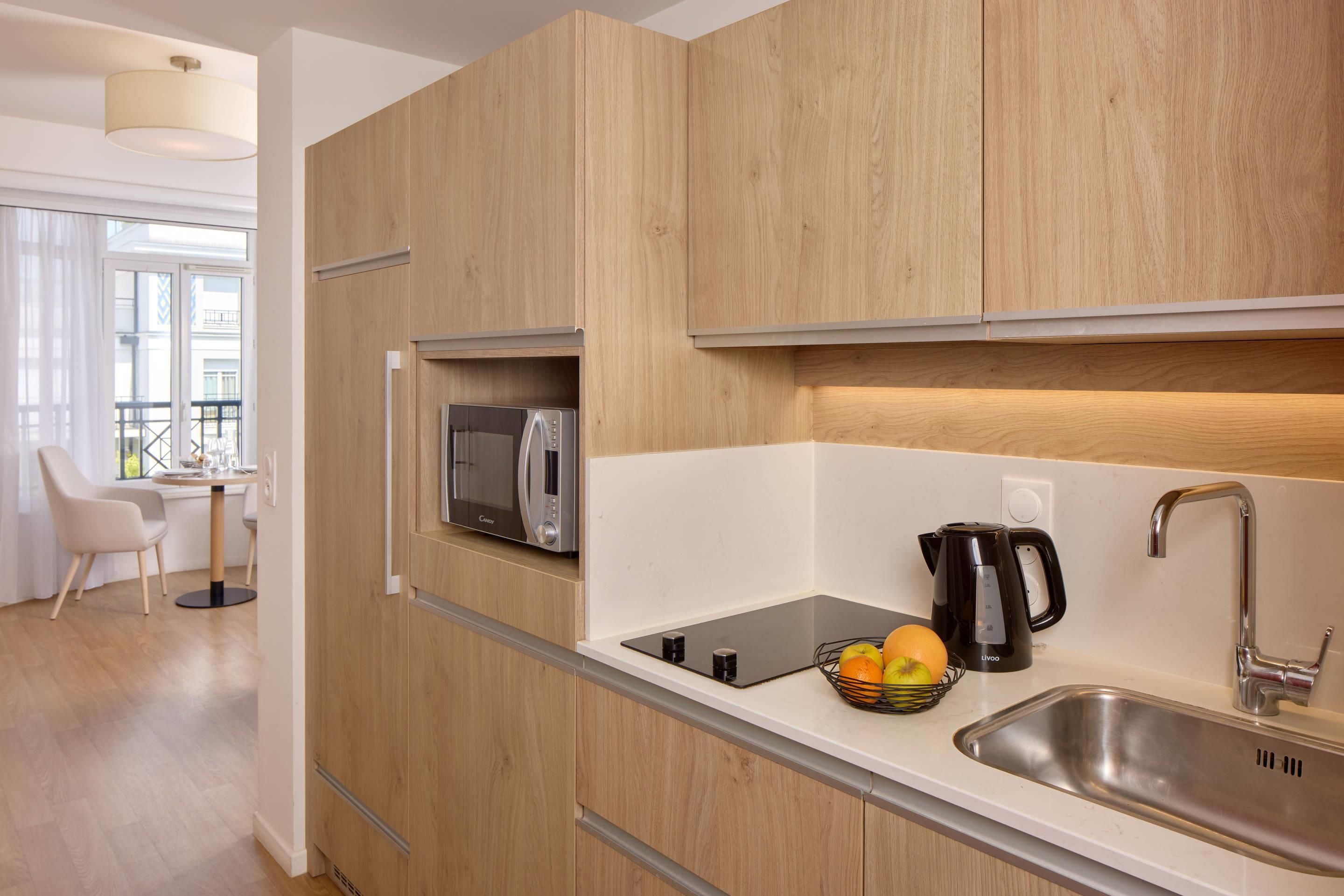 A modern kitchen with wooden cabinets, a built-in microwave, a kettle, and a fruit bowl.