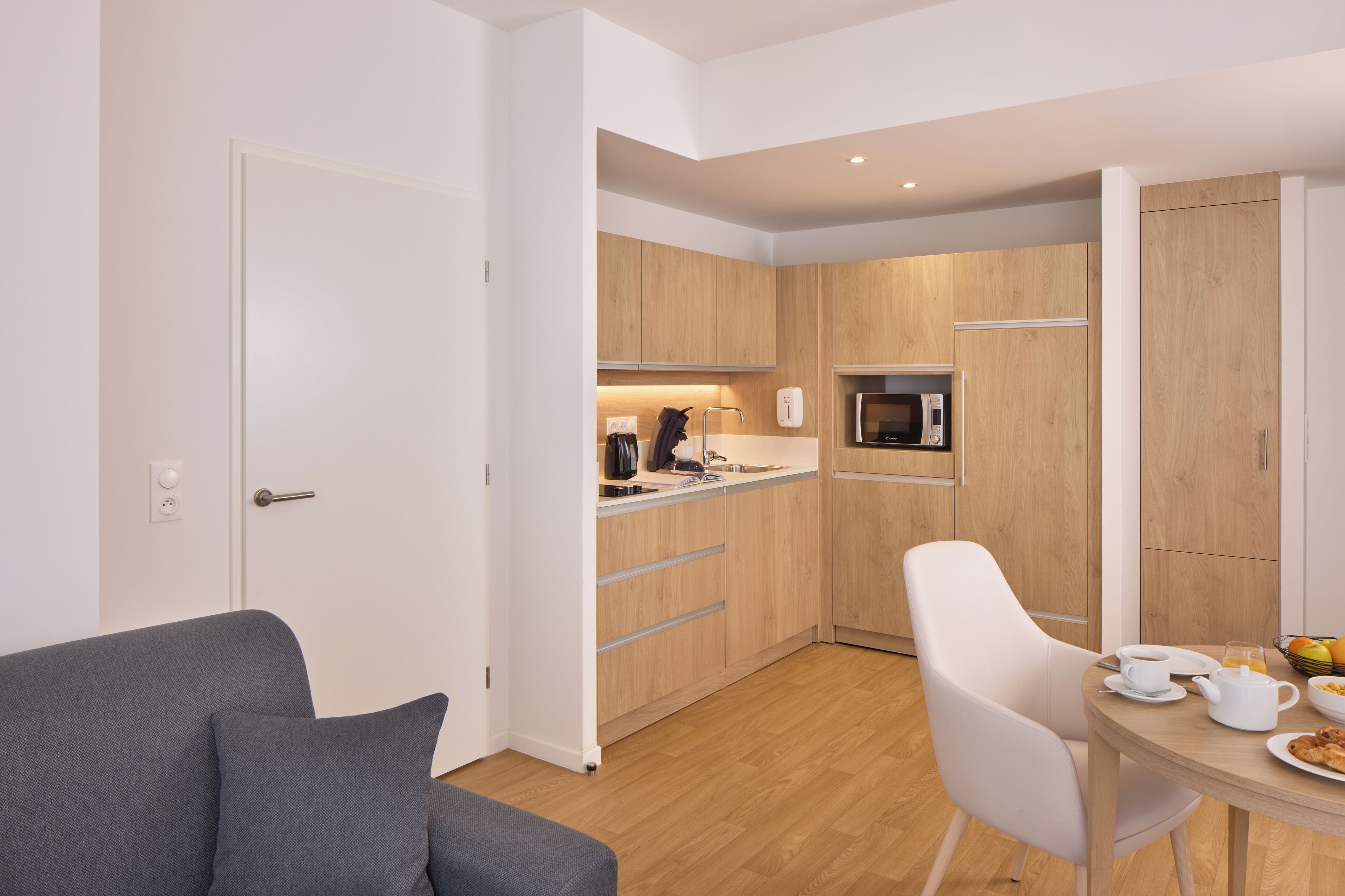 A modern kitchen with wooden cabinets, a microwave, and a dining area with a table set for breakfast.