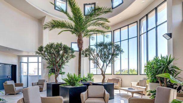 A spacious lounge area with wicker furniture, large windows, and potted plants. - Zenitude Hôtel-Résidences Val d'Europe (Chessy)