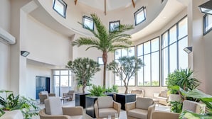 A spacious lounge area with wicker furniture, large windows, and potted plants. - Zenitude Hôtel-Résidences Val d'Europe (Chessy)
