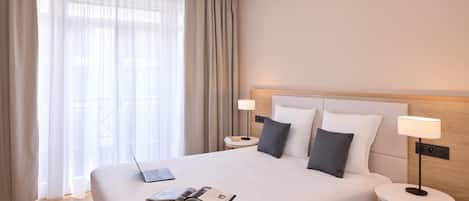 A hotel room with a large bed, two bedside tables, a laptop, and a book on the bed.
