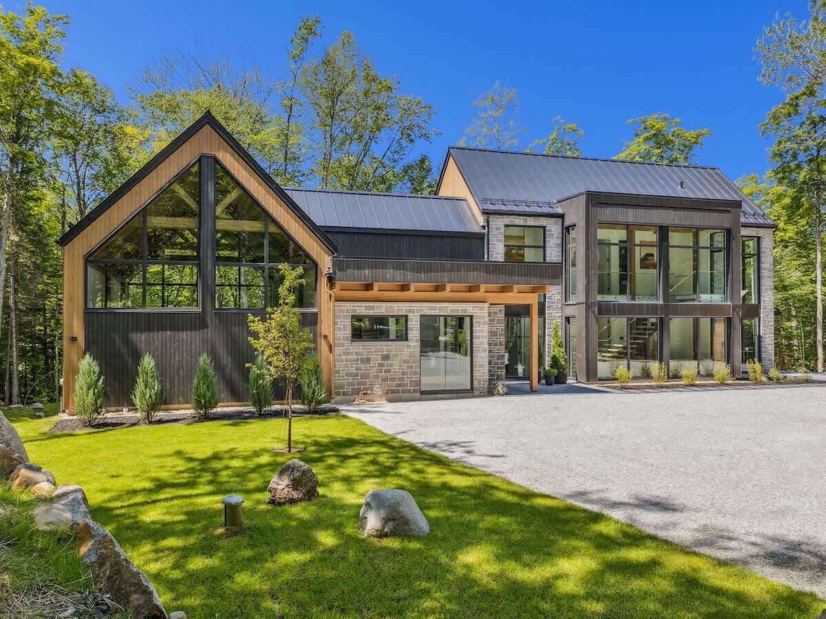 Une maison moderne à deux étages, dotée d’une grande façade vitrée, d’un revêtement extérieur en pierre et d’une pelouse bien entretenue.
