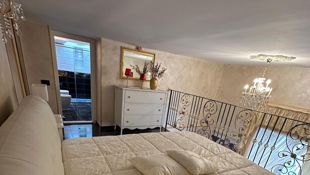 A bedroom with a large bed, a dresser, a mirror, and a balcony with a railing. - Luxury Apartment in Vomero (Naples)