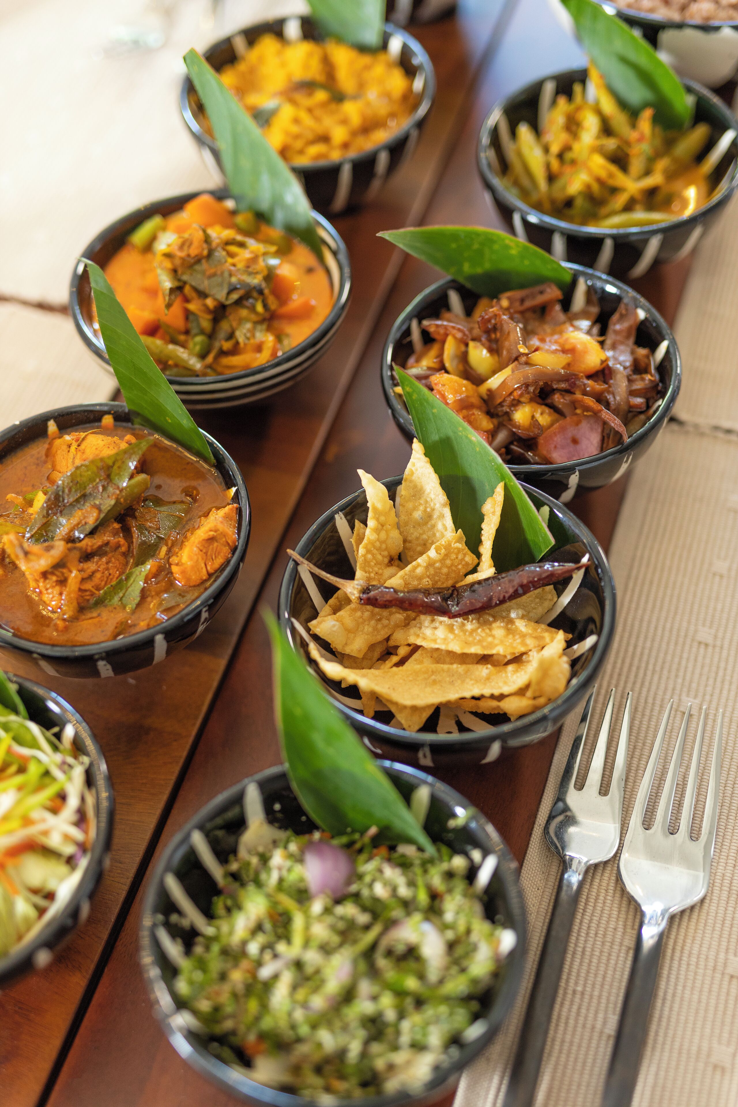A variety of dishes served in black bowls on a wooden table, accompanied by a fork and spoon set.