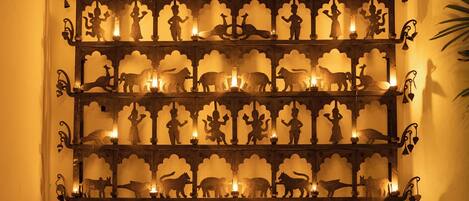 A decorative metal wall with animal and human silhouettes, each illuminated by a candle.