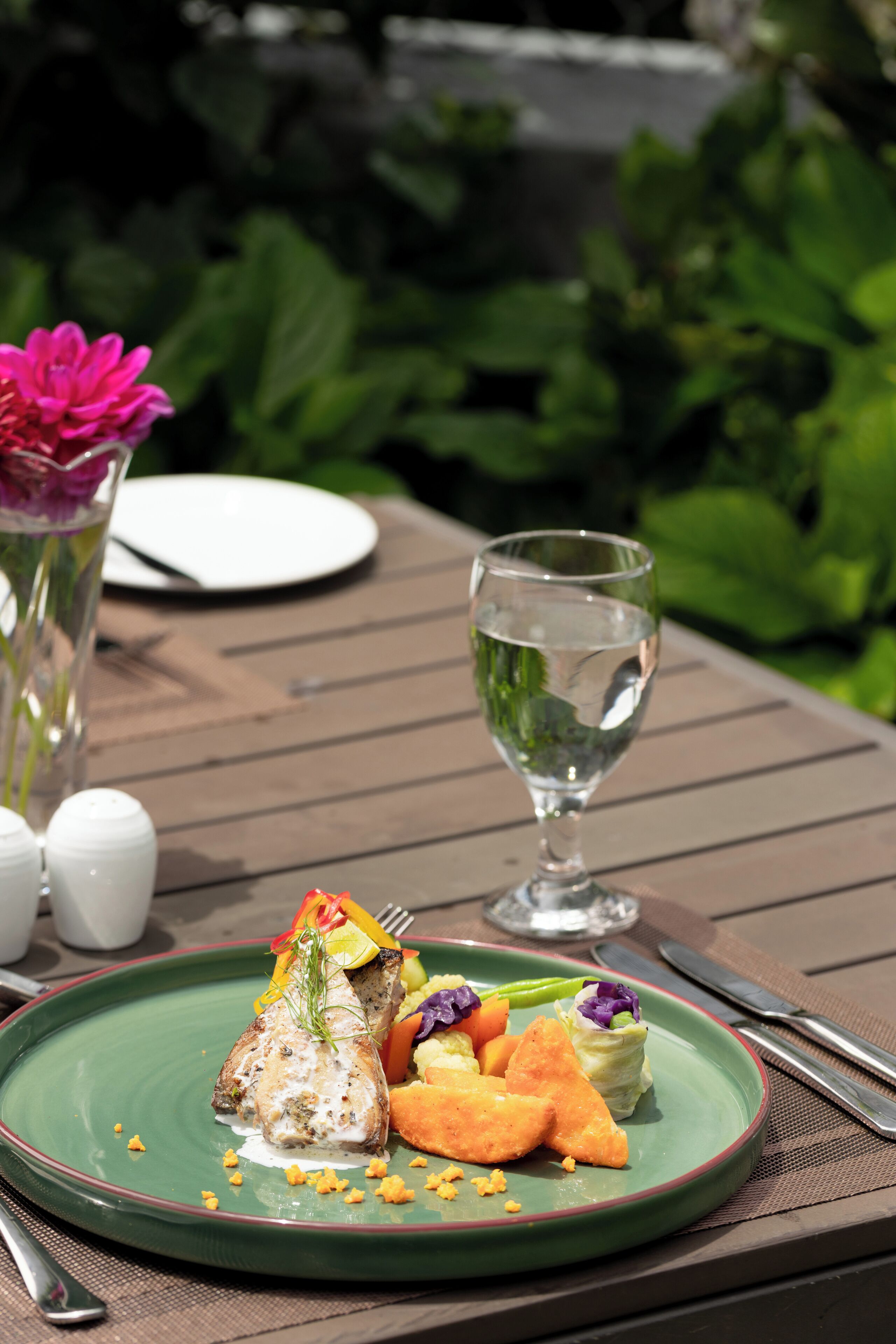 A green plate with a fish dish, vegetables, and a glass of water on a wooden table.