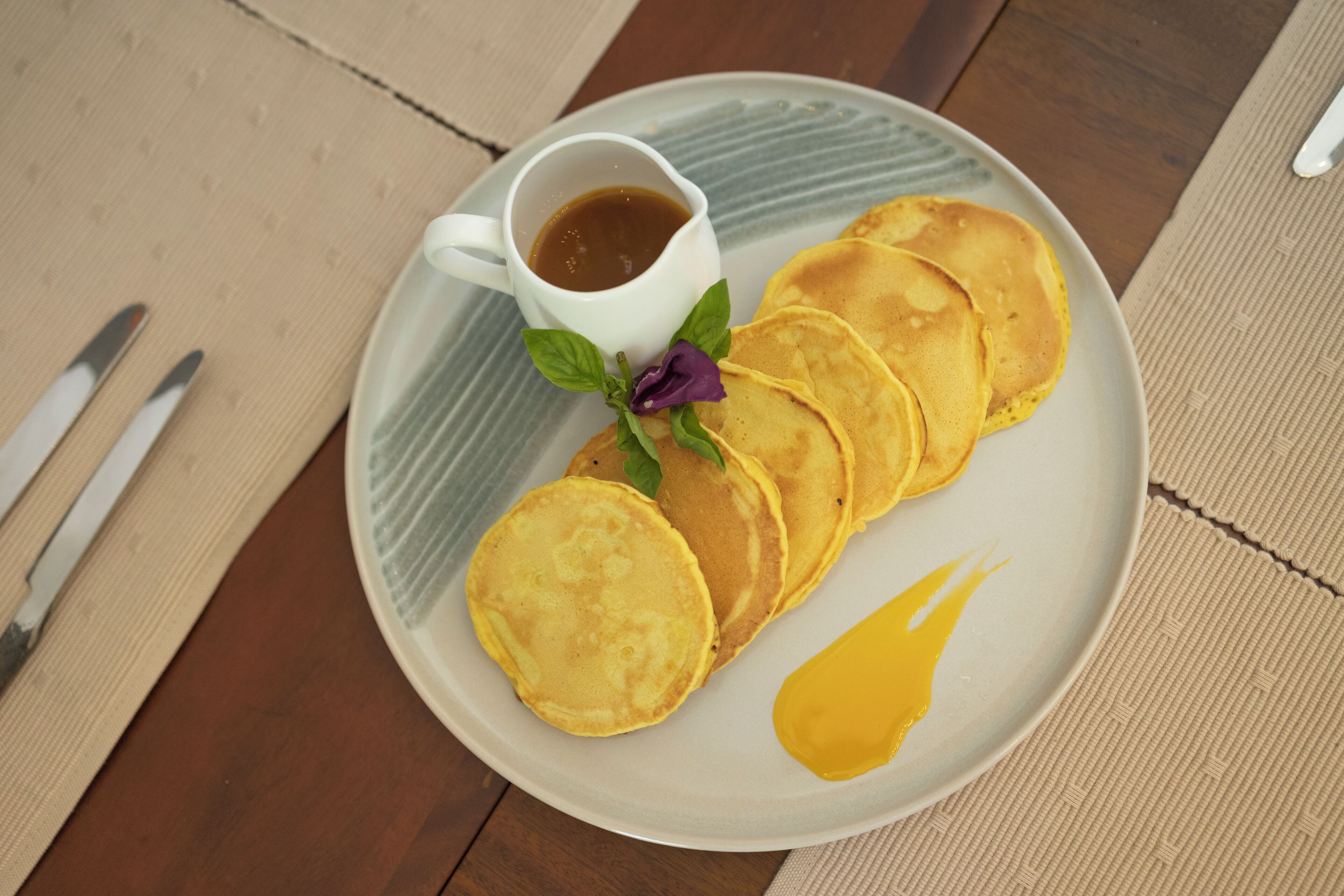 A plate with pancakes, syrup, and a small cup of syrup.