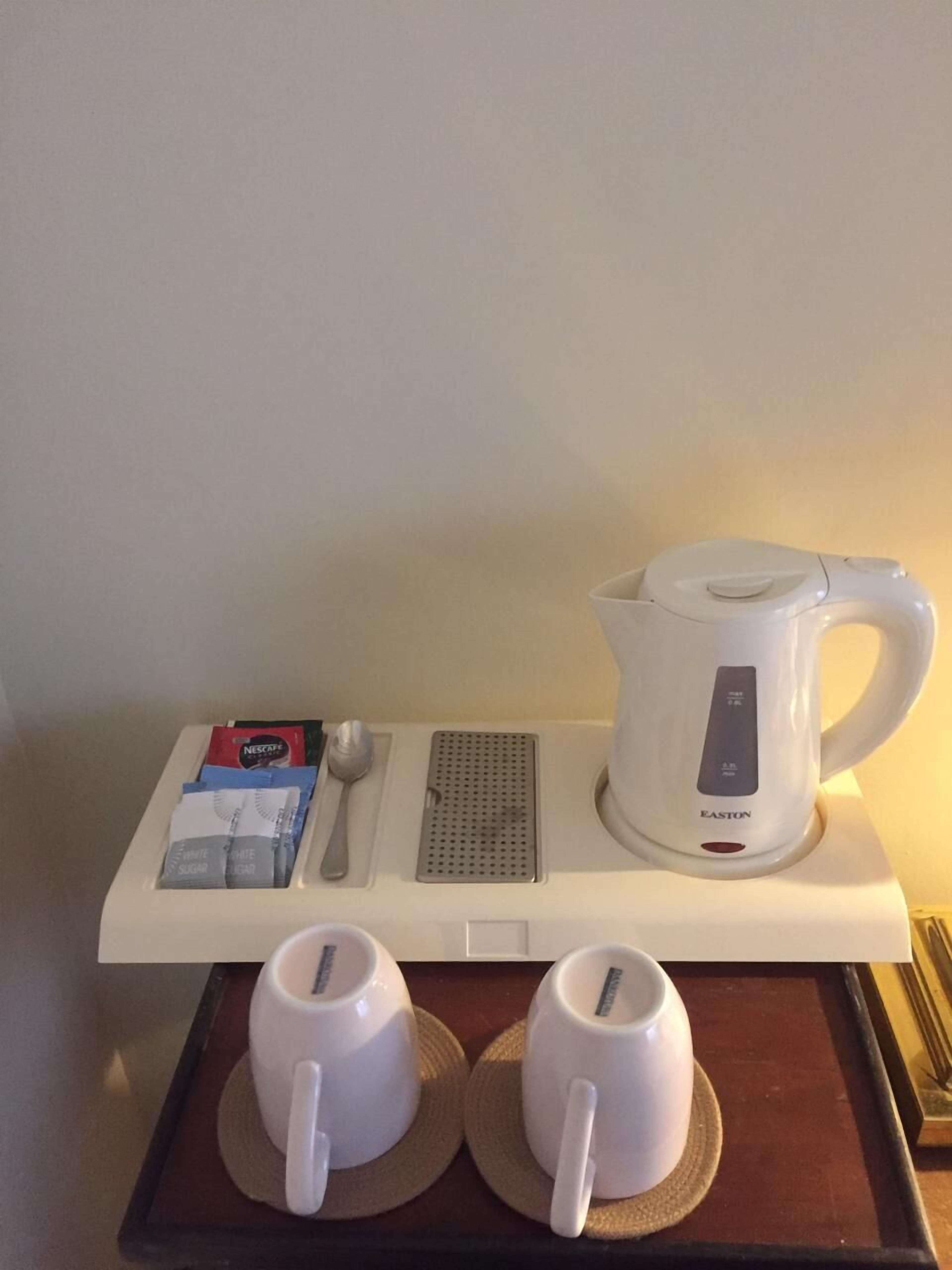 Un plateau de petit-déjeuner comprenant une bouilloire, deux tasses, une cuillère et un plateau.