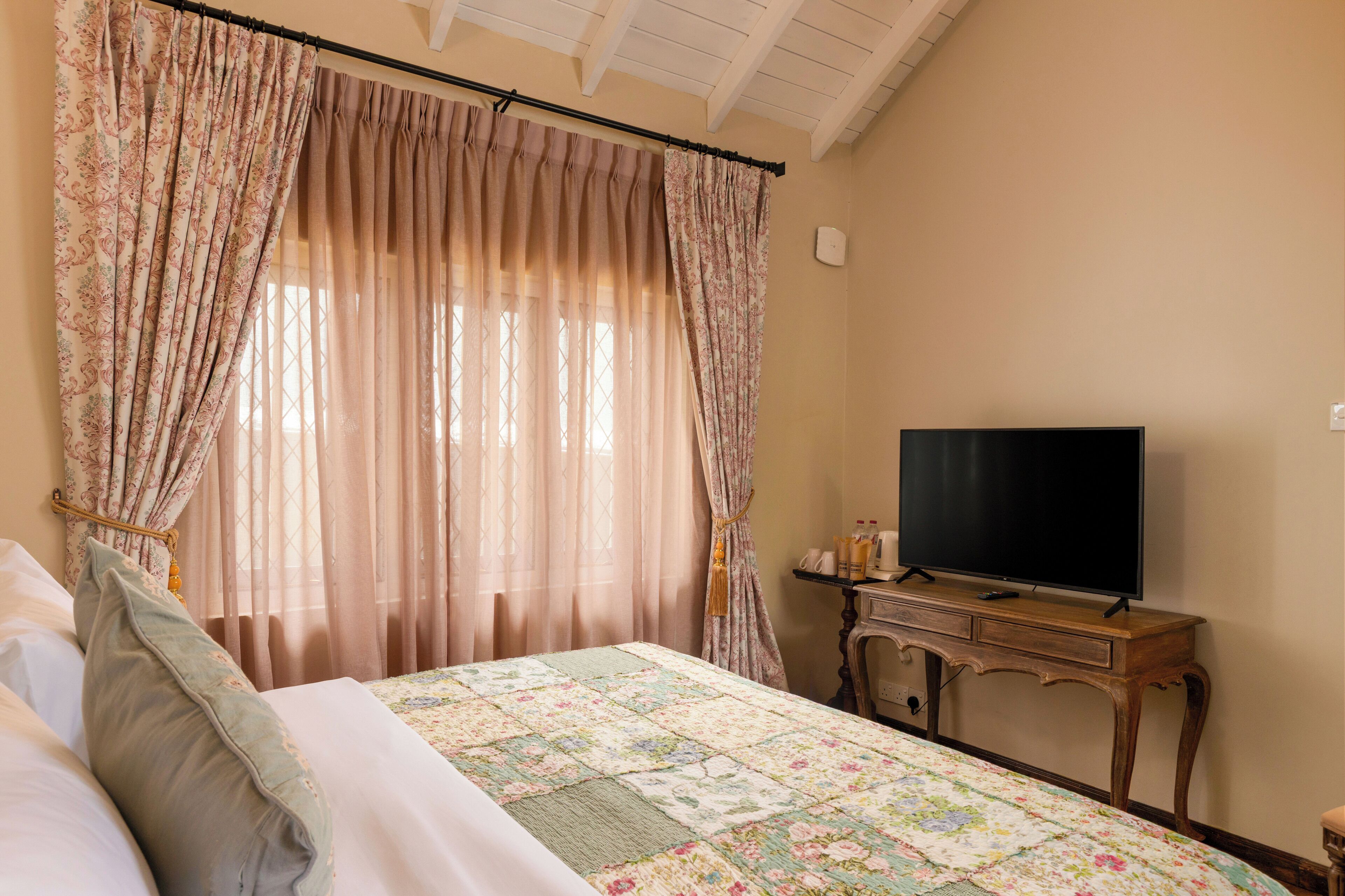 A bedroom with a bed, a television on a wooden stand, and a window with curtains.