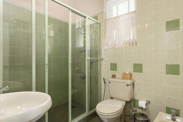 Un baño con ducha de vidrio, inodoro, lavamanos y ventana con cortina.