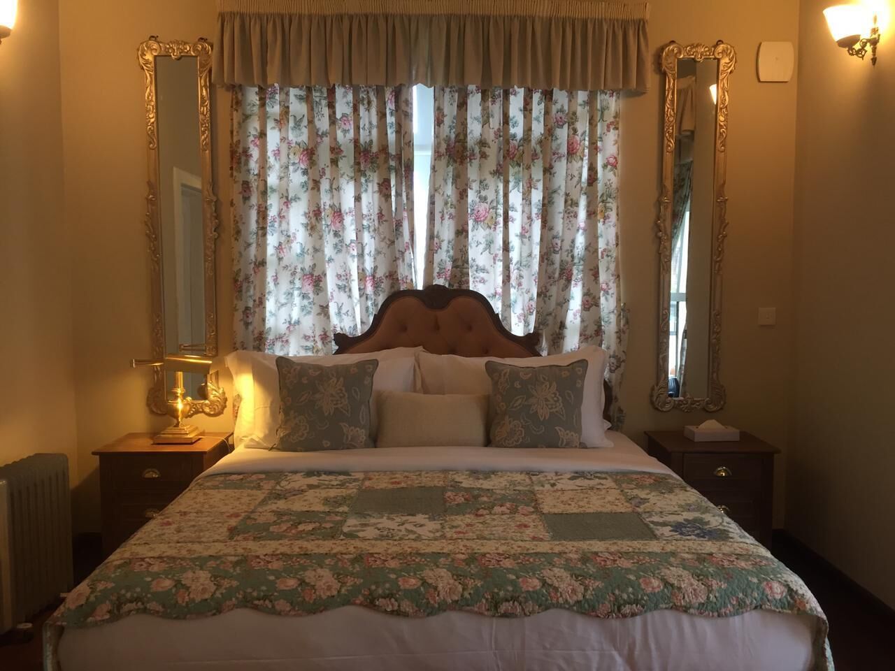 A neatly made bed with floral bedding, two bedside tables with lamps, and a large mirror on each side.