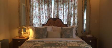 A neatly made bed with floral bedding, two bedside tables with lamps, and a large mirror on each side.