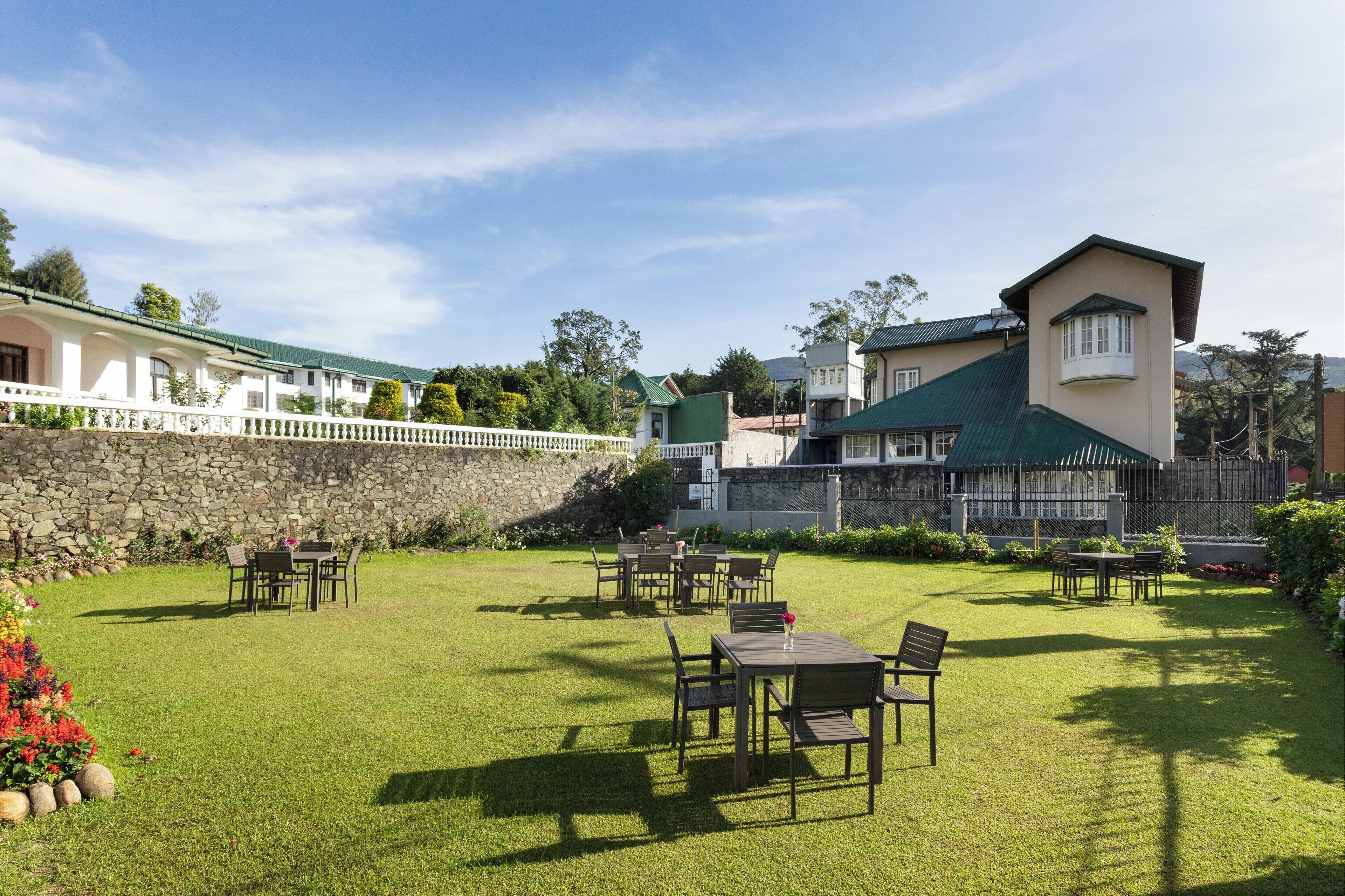 A well-maintained outdoor area with tables and chairs, a stone wall, and a building with a green roof.