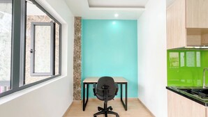 A compact kitchen with a teal wall, a wooden dining table, and a black office chair. - Tân Long Hotel (Ho Chi Minh City)