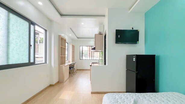 A modern hotel room with a large bed, a TV mounted on the wall, and a kitchen area visible through an open door. - Tân Long Hotel (Ho Chi Minh City)