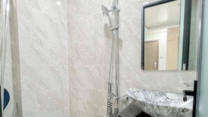 A bathroom with a white toilet, a shower with a handheld showerhead, a sink with a marble countertop, and a mirror above the sink. - Tân Long Hotel (Ho Chi Minh City)