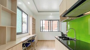 A modern kitchen with wooden cabinets, a green backsplash, and a window providing natural light. - Tân Long Hotel (Ho Chi Minh City)
