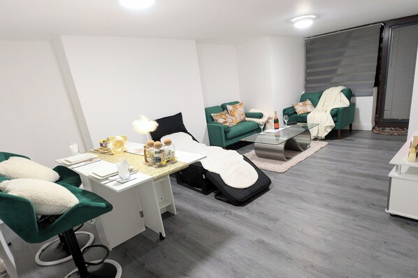 A modern living room with a green sofa set, a coffee table, and a small dining area with a white table and chairs.