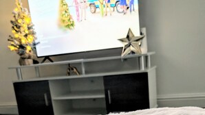 Huoneessa on valkoinen, pörröinen matto, ja seinällä on televisio, jonka näytöllä näkyy joulukuva.