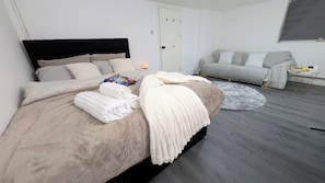 A modern bedroom with a large bed, a grey sofa, and a round rug.