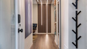 Un couloir au design moderne, avec un plancher en bois, une chaise noire et un luminaire vertical.