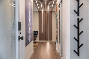 A hallway with a modern design, featuring a wooden floor, a black chair, and a vertical light fixture.
