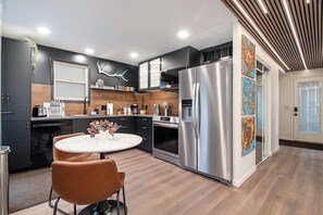 Een moderne keuken met een centraal eiland, roestvrijstalen apparatuur en een eethoek met een ronde tafel en stoelen.