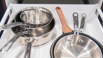 A drawer with kitchen utensils including a pot, a pan, and a wooden-handled utensil.