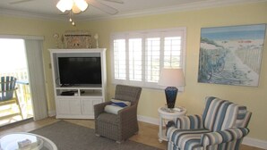 A living room with a television, two chairs, a coffee table, and a painting on the wall. - Panoramic Oceanfront Condo | Balcony +Beach Access (Saint Augustine)