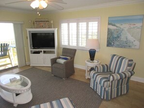 A living room with a television, two chairs, a coffee table, and a painting on the wall. - Panoramic Oceanfront Condo | Balcony +Beach Access (Saint Augustine)