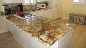 A kitchen with white cabinets, a granite countertop, a microwave, a toaster, and a refrigerator. - Panoramic Oceanfront Condo | Balcony +Beach Access (Saint Augustine)