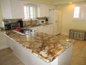 A kitchen with white cabinets, a granite countertop, a microwave, a toaster, and a refrigerator. - Panoramic Oceanfront Condo | Balcony +Beach Access (Saint Augustine)