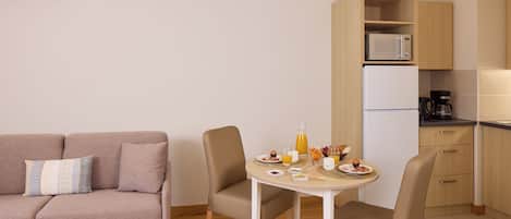 A compact living space with a sofa, a dining table with chairs, a kitchen area with a microwave and refrigerator, and a coffee maker.