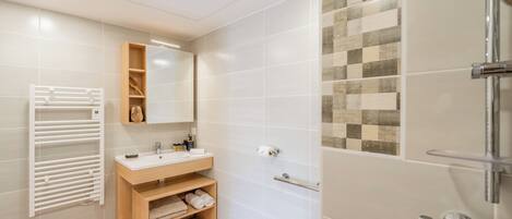 A modern bathroom with a white sink, wooden vanity, and a glass shower enclosure.
