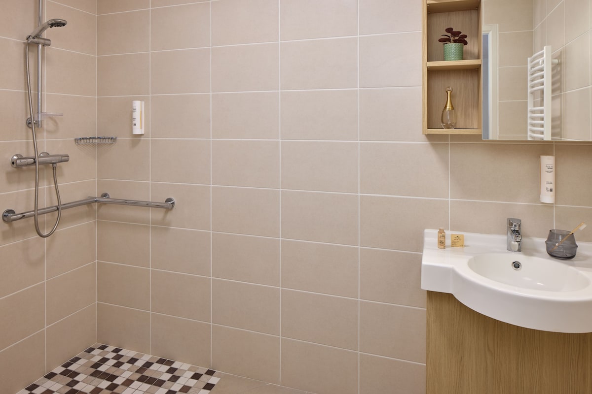 A bathroom with a shower, a sink, and a shelf with toiletries.