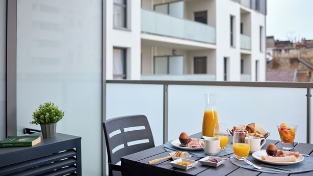 Ein Balkon mit Frühstücksangebot, darunter ein Tisch mit Tellern, Gläsern und einer Saftflasche.