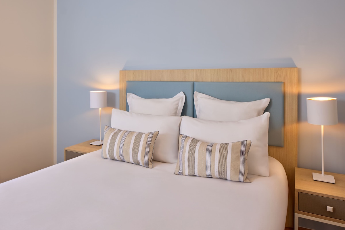 A neatly made bed with white linens, two bedside lamps, and striped pillows.