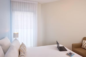 A hotel room with a bed, a laptop, a lamp, and a window with sheer curtains. - Quality Aparthotel Pau Porte des Pyrénées (Pau)