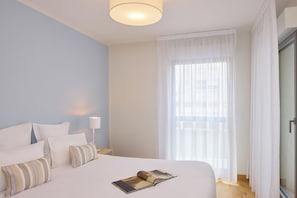 A hotel room with a large bed, a bedside lamp, and a window with sheer curtains. - Quality Aparthotel Pau Porte des Pyrénées (Pau)