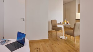 Ein Hotelzimmer mit Holzboden, einer weißen Tür, einem Laptop auf einem kleinen Tisch und zwei Stühlen um einen kleinen Tisch mit einer Lampe.