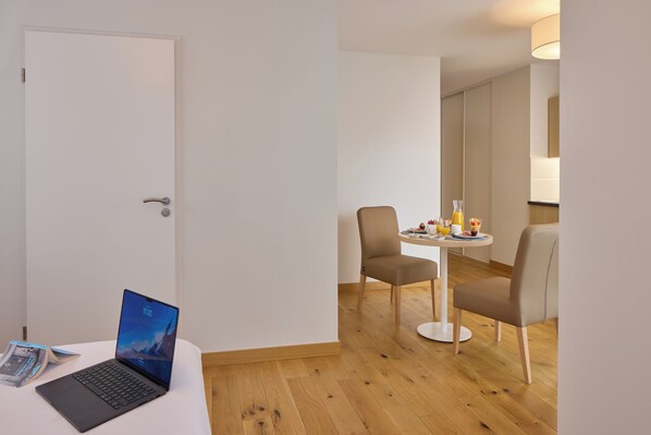 A hotel room with a wooden floor, a white door, a laptop on a small table, and two chairs around a small table with a lamp. - Quality Aparthotel Pau Porte des Pyrénées (Pau)