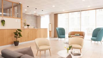 Een moderne hotellobby met een receptiebalie, zithoek en grote ramen.