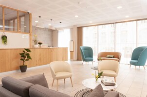 Un moderno vestíbulo de hotel con una recepción, zona de estar y grandes ventanales.