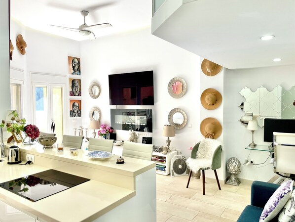 Une cuisine moderne dotée d’un îlot central, un coin repas avec un canapé et un salon avec une télévision et des objets de décoration.