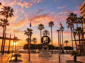 A sunset view with palm trees, a statue, and flags.