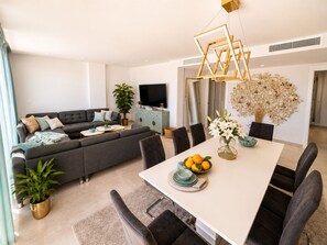 Una sala de estar moderna con sofá, televisor, mesa de comedor, sillas y plantas decorativas.