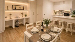 Un espace de repas moderne avec une table dressée pour quatre personnes, une cuisine avec des meubles blancs et un luminaire suspendu au-dessus de la table.