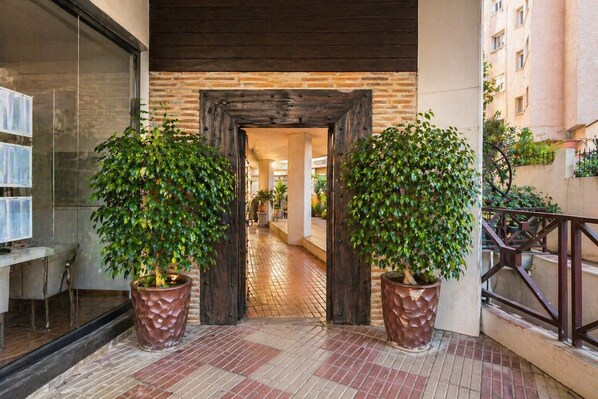 A corridor with a wooden door, potted plants, and a tiled floor.