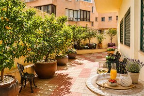 A courtyard with potted plants, outdoor seating, and a tiled floor.
